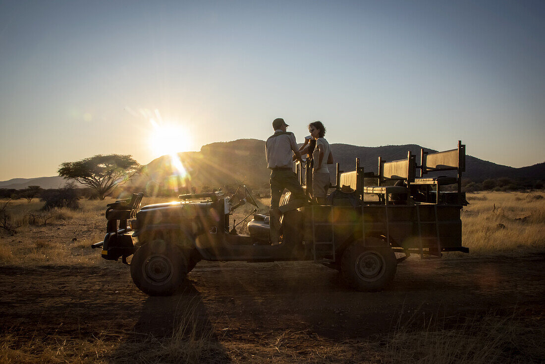 Safari-Führer im Gespräch mit Gästen, während er in einem Jeep in der Savanne der Gabus Game Ranch bei Sonnenaufgang steht; Otavi, Otjozondjupa, Namibia.