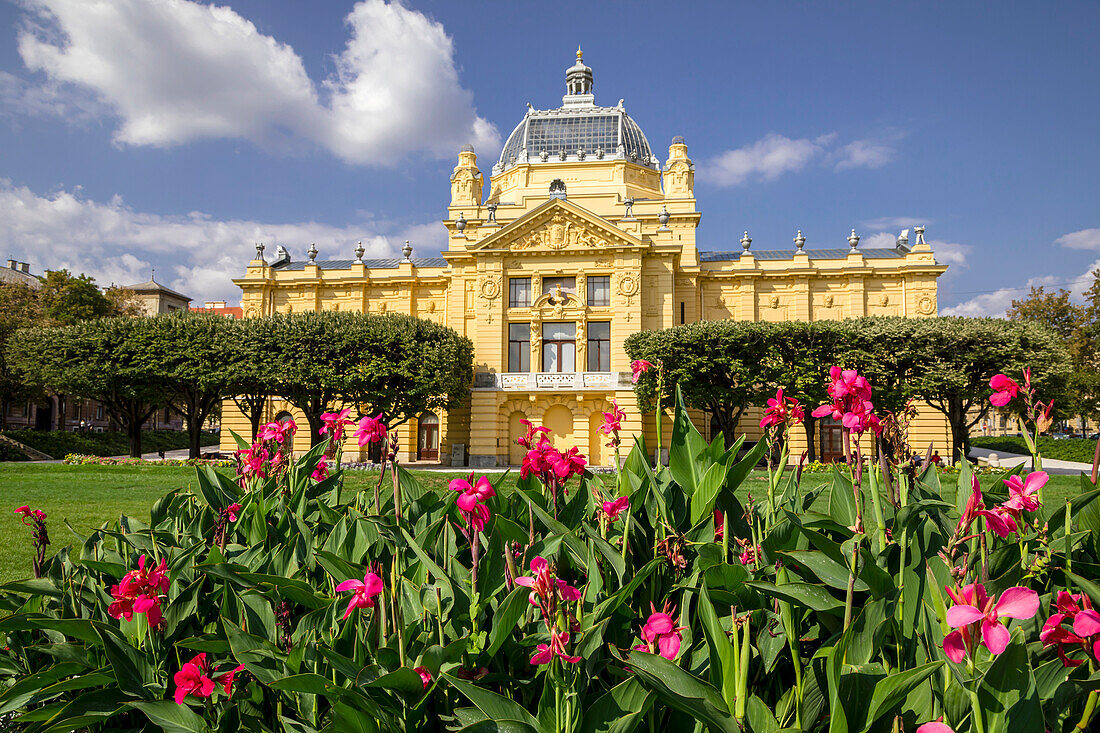 Colorful flower bed in front of the yellow stone facade of the Art Pavilion in Zagreb on the Lenuci Horseshoe, Lower Town area at King Tomislav Square; Zagreb, Croatia