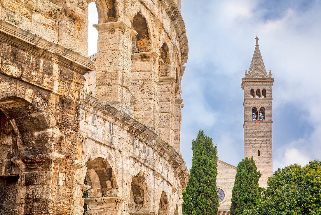 Die Arena von Pula, 1. Jahrhundert, römisches Amphitheater und der Glockenturm der Kirche und des Klosters des Heiligen Antonius von Padua im Hintergrund mit blauem Himmel; Pula, Istrien, Kroatien.