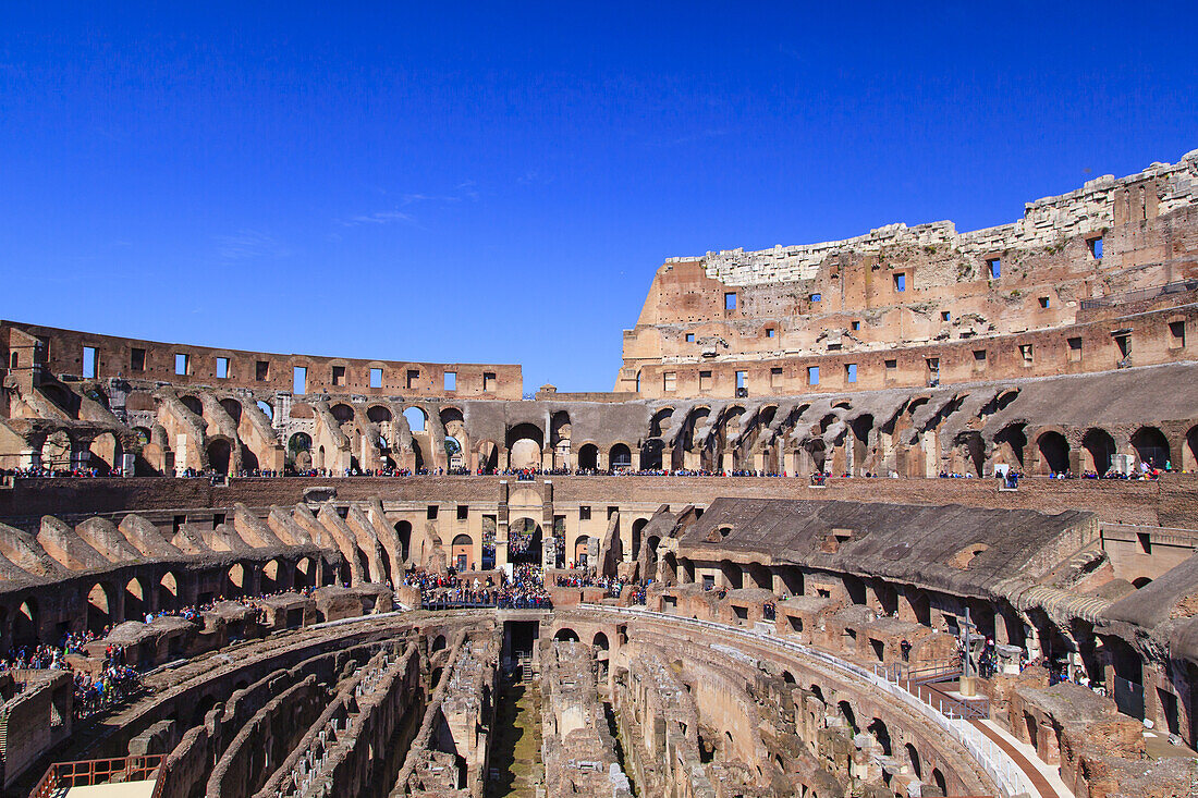 Overview of the inside of the iconic Colosseum against a blue sky with crowds of tourists sightseeing; Rome, Lazio, Italy