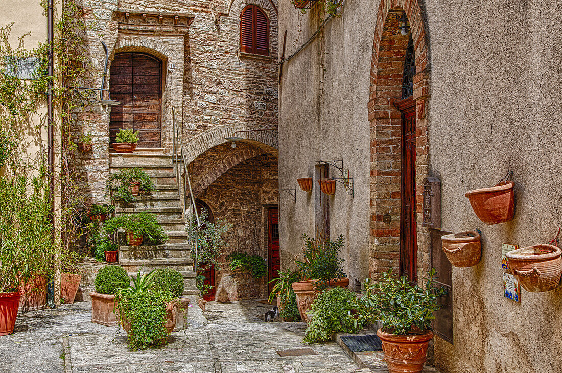Außenansicht eines alten Steingebäudes mit einer Treppe und drei Eingängen zu separaten Wohnungen mit Terrakotta-Blumentöpfen auf der Terrasse sowie an den Steinwänden; Volterra, Provinz Pisa, Toskana, Italien.