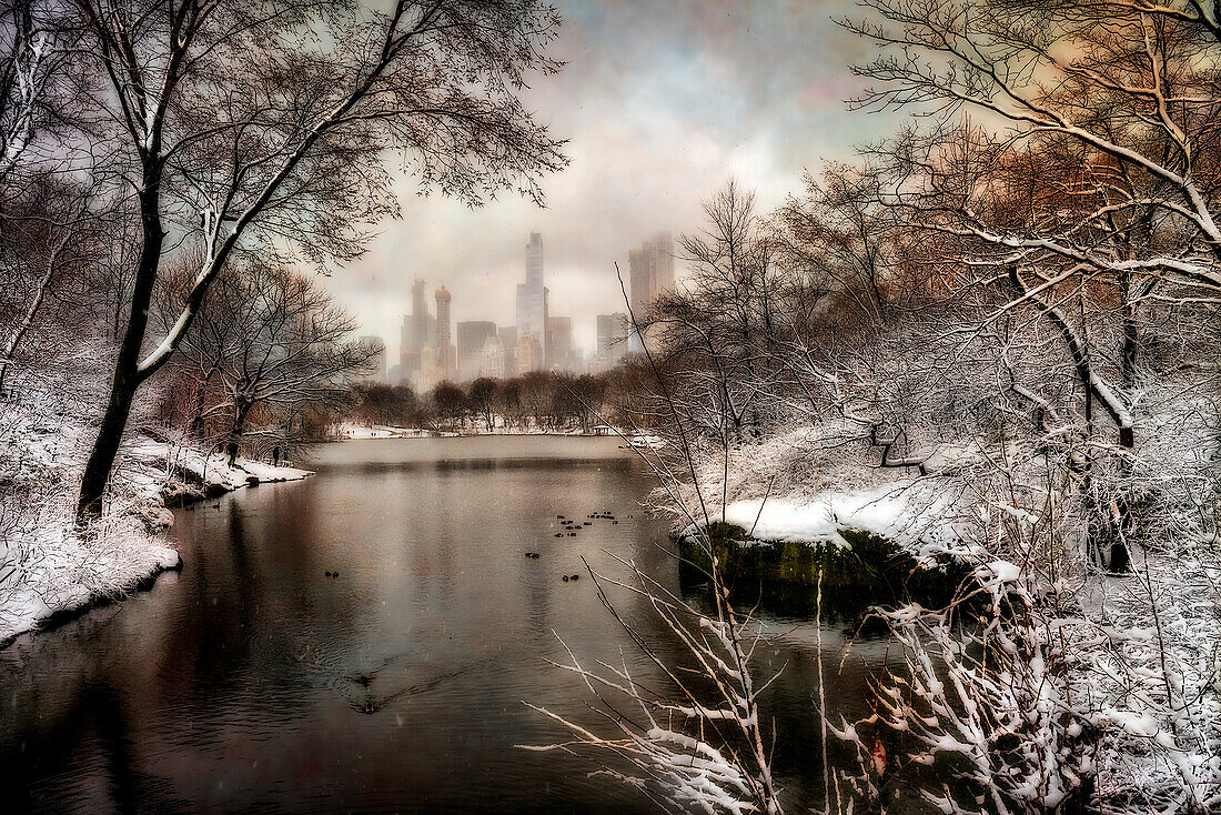 View of the city through the snow covered trees and shoreline around The Lake in Central Park; New York City, New York, United States of America