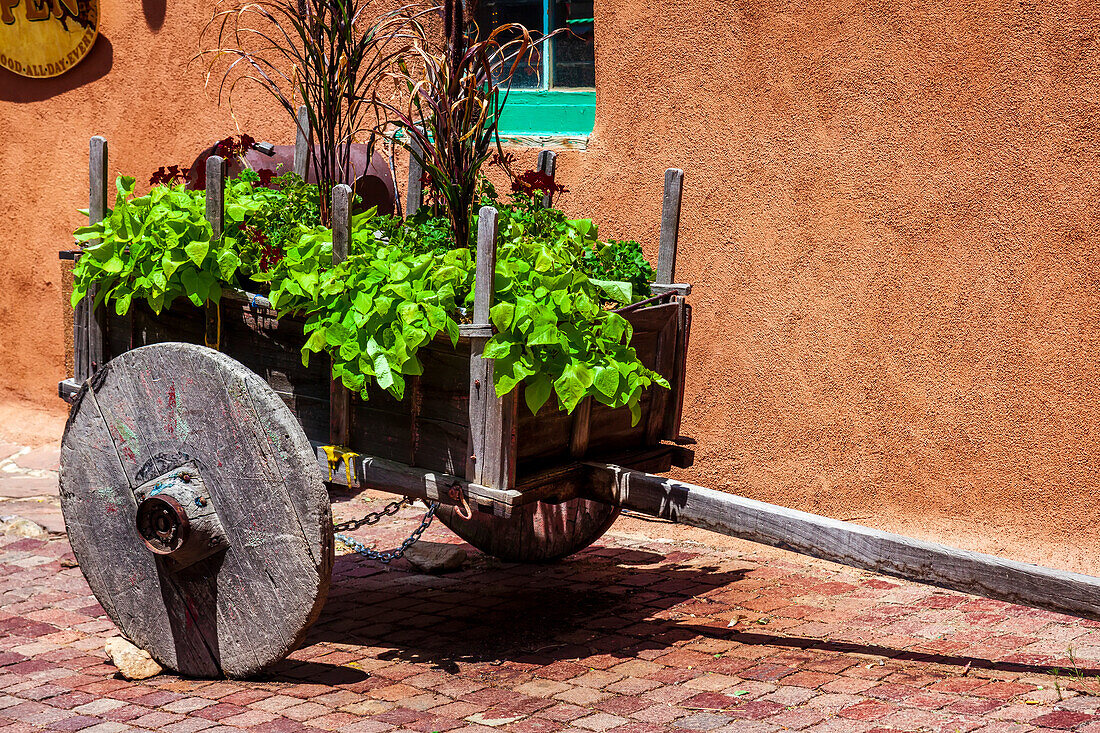 A wooden, wagon planter adorns the cobblestone streets outside of a building in the old town of Taos; Taos, New Mexico, United States of America