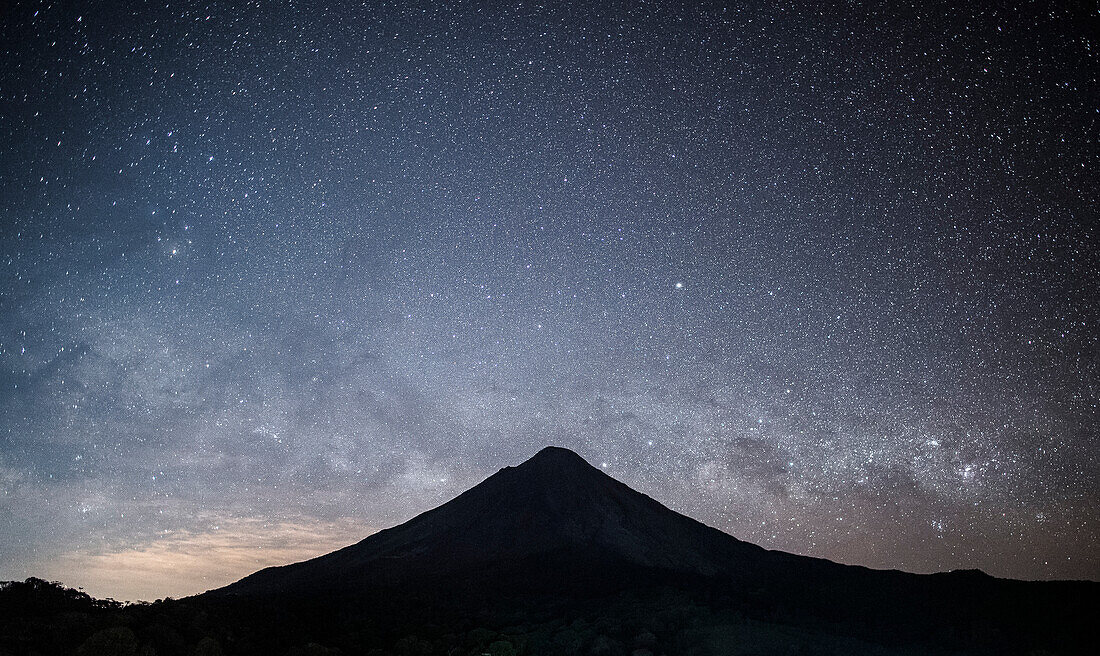 The Milky Way galaxy rises above a dramatic silhouette of the Arenal Volcano, an active stratovolcano; Alajuela Province, Costa Rica