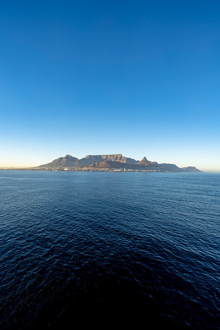 Dramatischer Blick auf Devil's Peak, Tafelberg, Lion's Head und die Hafenstadt Kapstadt in der Morgendämmerung vom Meer aus; Kapstadt, Kapprovinz, Südafrika