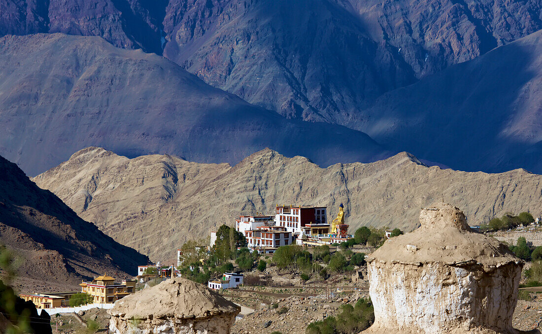 Looking through the mud-covered rooftops of the stupas down to the rooftops of the Likir Monastery with its gold plated statue of a seated Buddha above the Indus Valley, in the Himalayan Mountains of Kadakh, Jannu and Kashmir; Likir, Ladakh, India