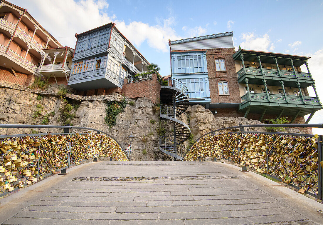 Traditional Georgian architecture in Legvtakhevi, part of the historical neighborhood of Abanotubani in the Old Town, crossing a small arch bridge with love locks attached to its railings; Tbilisi, Georgia