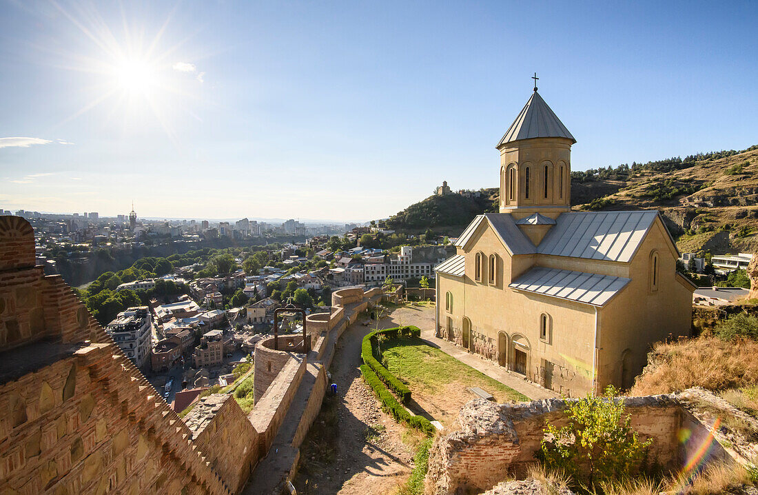 St Nicholas Church, 20th Century restoration, on the lower court of the ancient walled fortress of Narikala located on the hillside on the left bank above the Kura (Mtkvari River) with a bright sun and blue sky; Tbilisi, Georgia