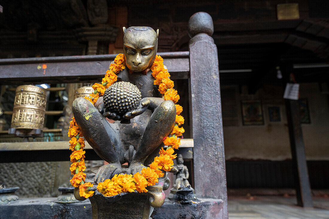 Brass monkey figure decorated with flower garland in Kwa Bahal Golden Temple in the old city of Patan or Lalitpur built in the twelfth century by King Bhaskar Varman in the Kathmandu Valley; Patan (Lalitpur), Kathmandu Valley, Nepal