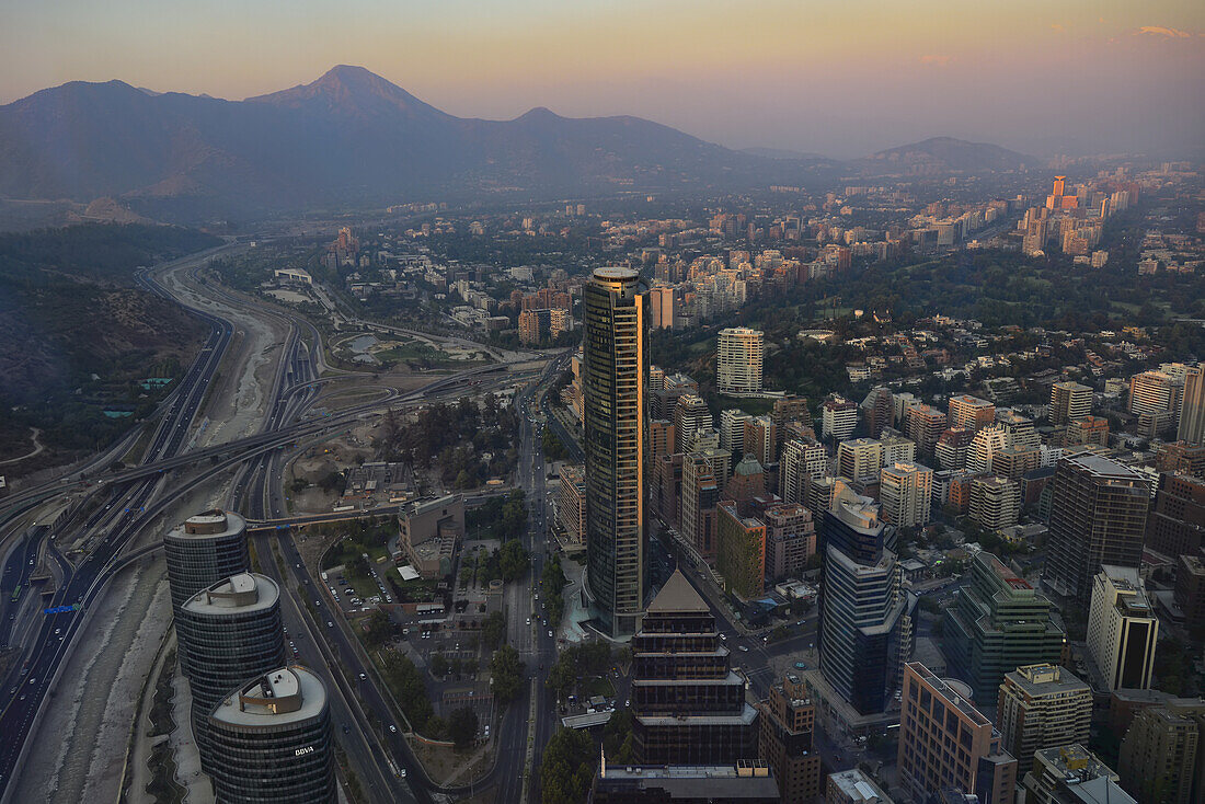 Evening view over Santiago with the sunset reflecting on the second tallest skyscraper of the country, Titanium La Portada and the River Mapocho running through the City Center; Santiago de Chile, Chile