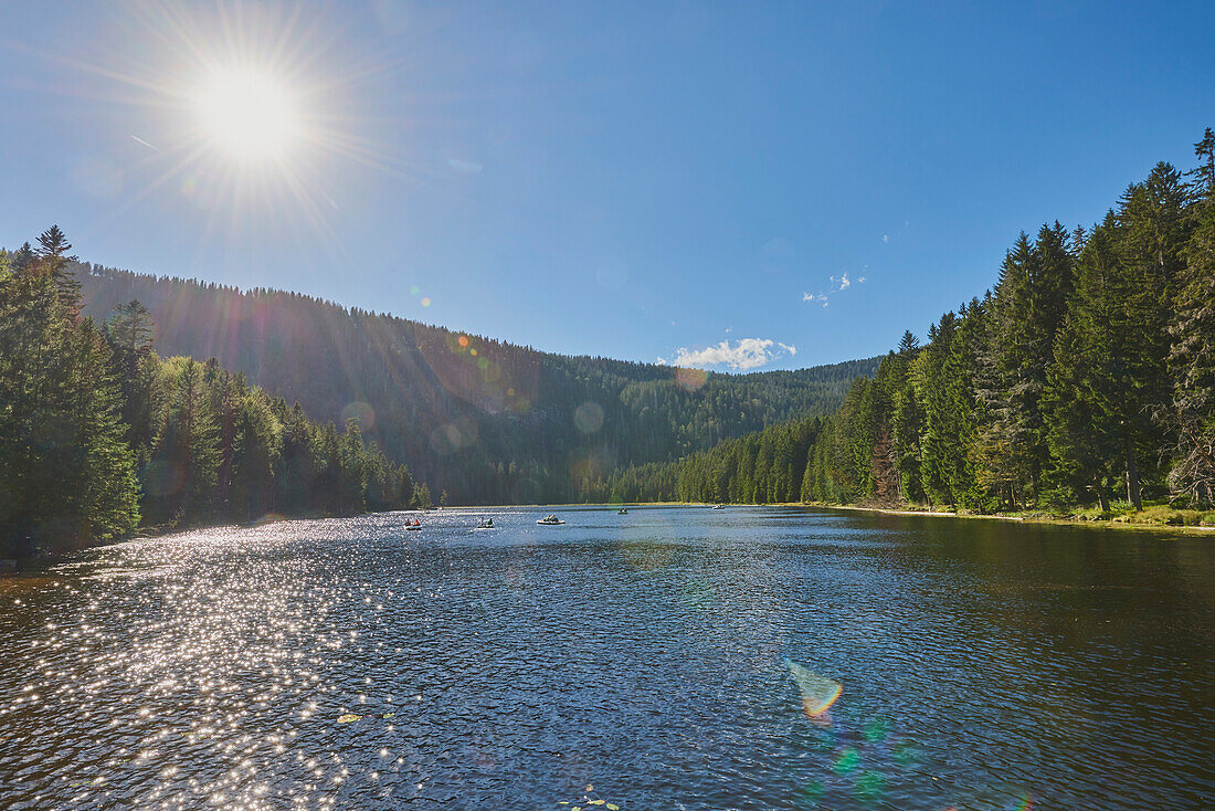 Sonnenaufgang über dem Arbersee mit Menschen in Booten auf dem Wasser im Nationalpark Bayerischer Wald; Bayern, Deutschland