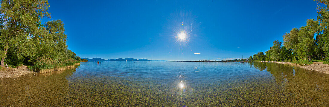 Chiemsee mit Sonnenaufgang am blauen Himmel an einem sonnigen Tag; Bayern, Deutschland