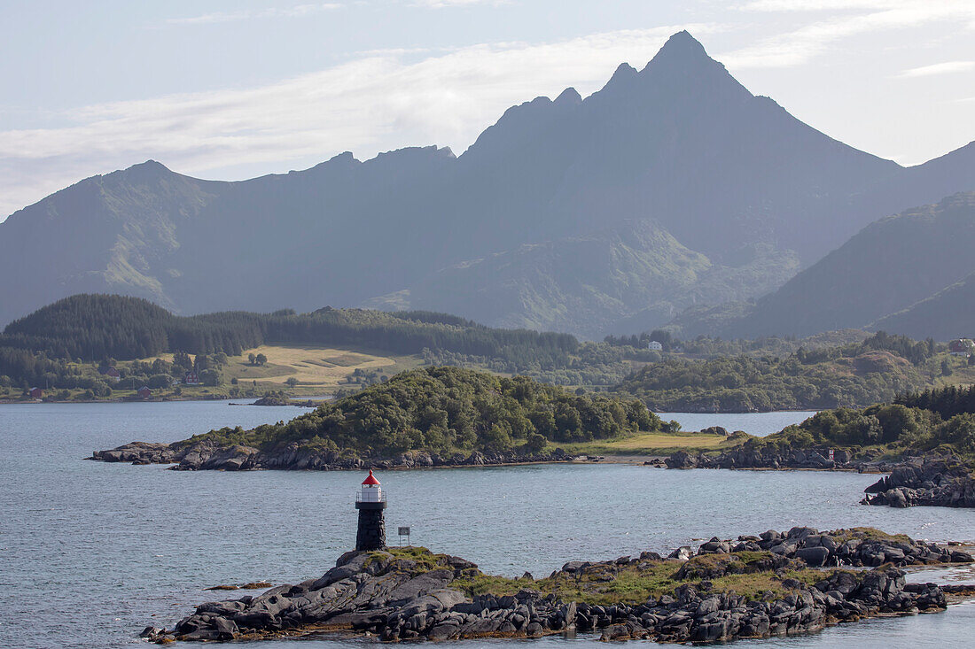 Buksnes Lighthouse at the remote settlement of Gravdal on the island of  Vestvagoya with silhouetted mountain peaks in the distance on the Lofoten Islands; Lofoten, Nordland, Norway