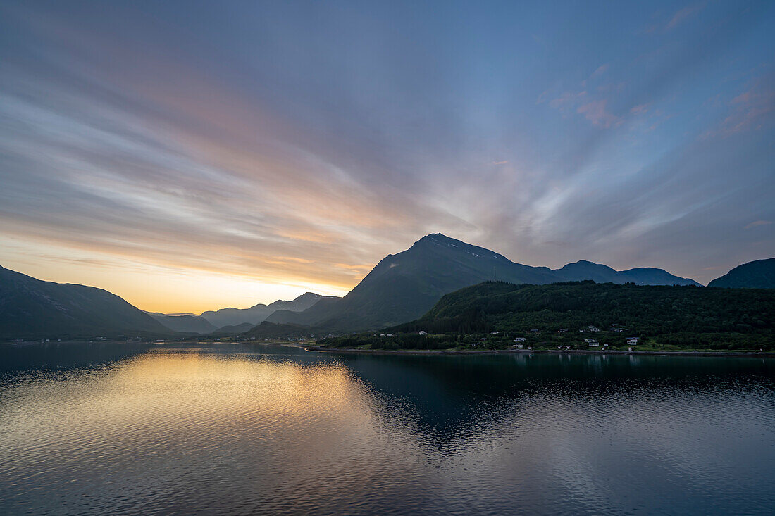 Mitternachtssonne mit einem dramatischen Himmel in der Dämmerung, gesehen von einem Kreuzfahrtschiff in den Fjorden; Westfjorde, Norwegen