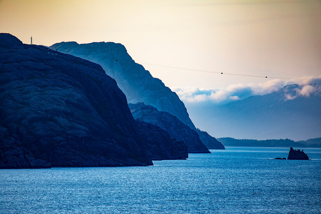 Silhouette von Berggipfeln und Inseln mit Stromleitungen, die sich über die Wasserwege in der Sommerlandschaft in den Westfjorden von Norwegen erstrecken; Sogn og Fjordane, Vestland, Norwegen