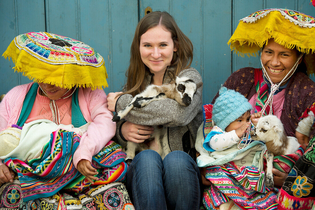 Eine junge Frau hält eine Ziege und sitzt zwischen zwei peruanischen Frauen; Cusco Peru