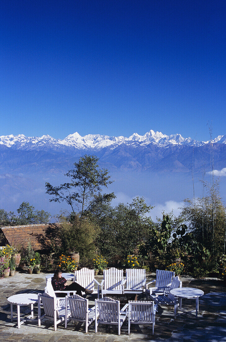 Nepal, Nagarkot, Frau sitzt im Hof eines Fort-Hotels, im Hintergrund Fernsicht auf das Zentralhimalaya-Gebirge.