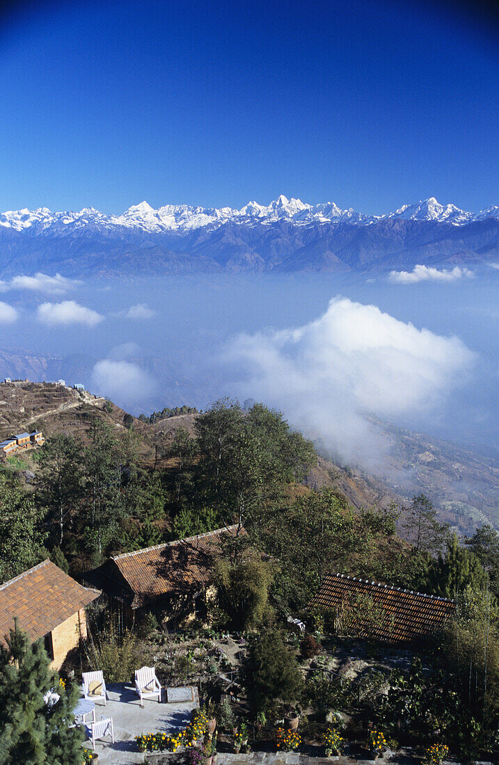 Nepal, Overview of Fort Hotel on hillside and clouds with himalayan mountains in background; Nagarkot