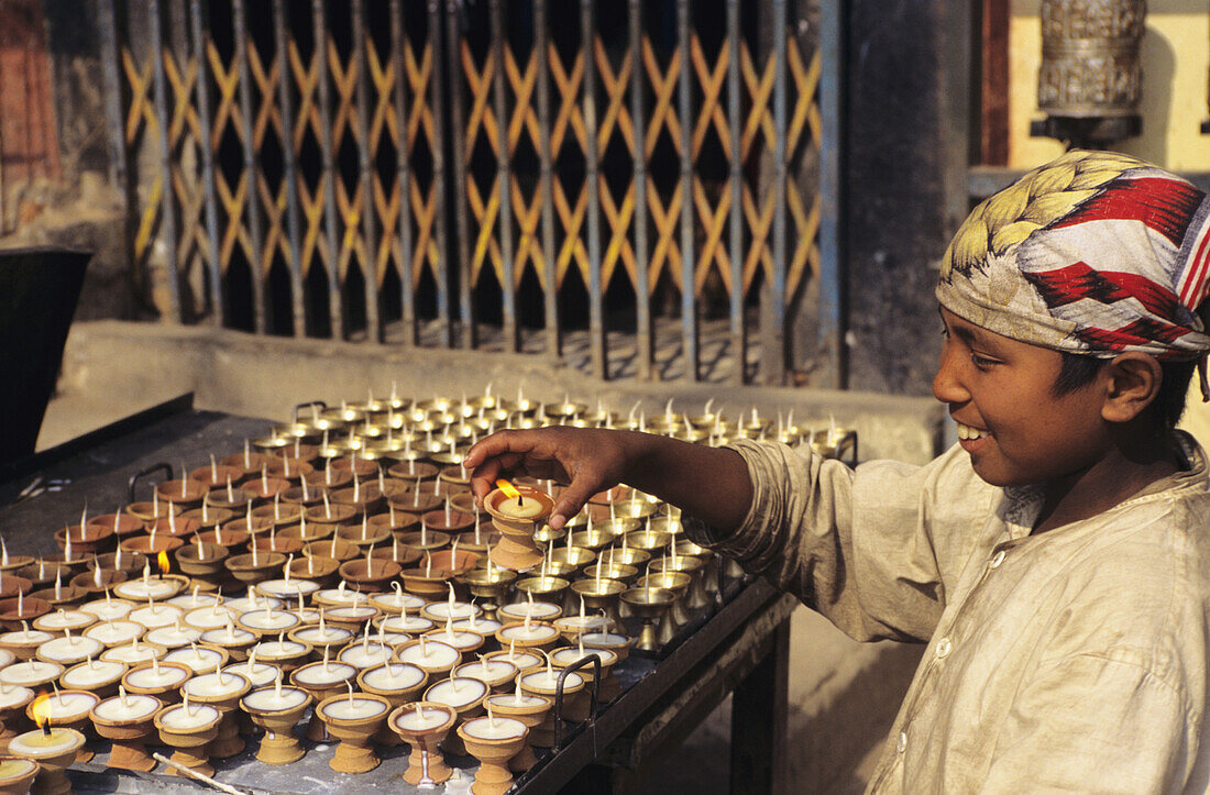 Nepal, Kathmandu, Lächelnder einheimischer Junge zündet religiöse Kerzen an, Blick von der Seite.