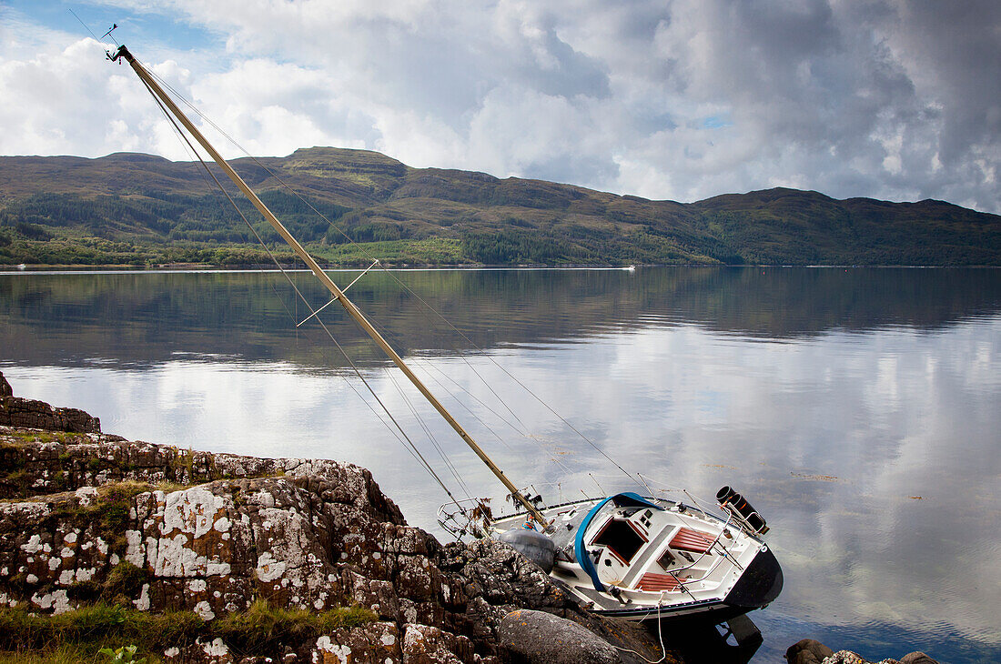 Ein Boot im Wasser, das sich auf der Seite gegen das Ufer lehnt; Argyll Schottland