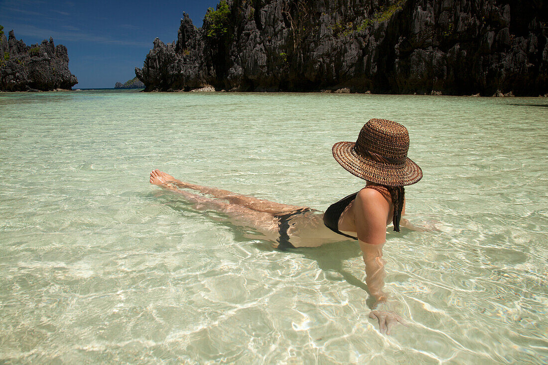 Eine Touristin mit Sonnenhut und Bikini entspannt sich im klaren Wasser der Insel Matinloc bei El Nido und Corong Corong; Bacuit Archipel; Palawan Philippinen