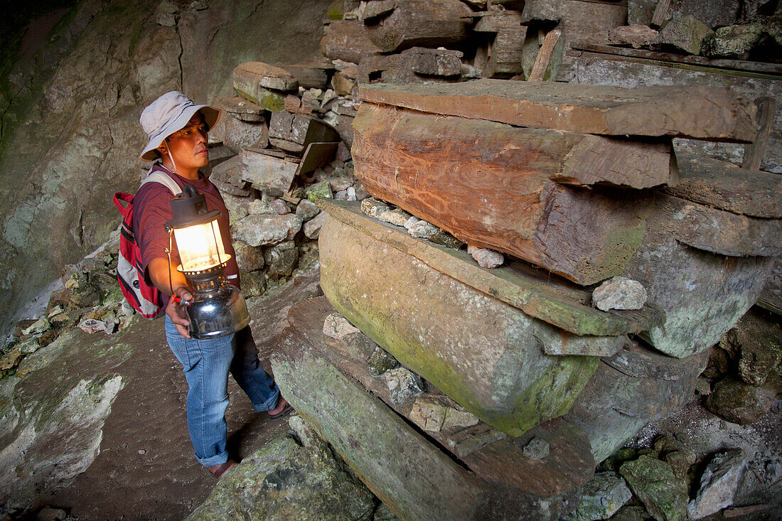 A Tour Guide Uses A Lantern To Look At The Many Coffins In The Entrance To Lumiang Burial Cave Near Sagada; Luzon Philippines