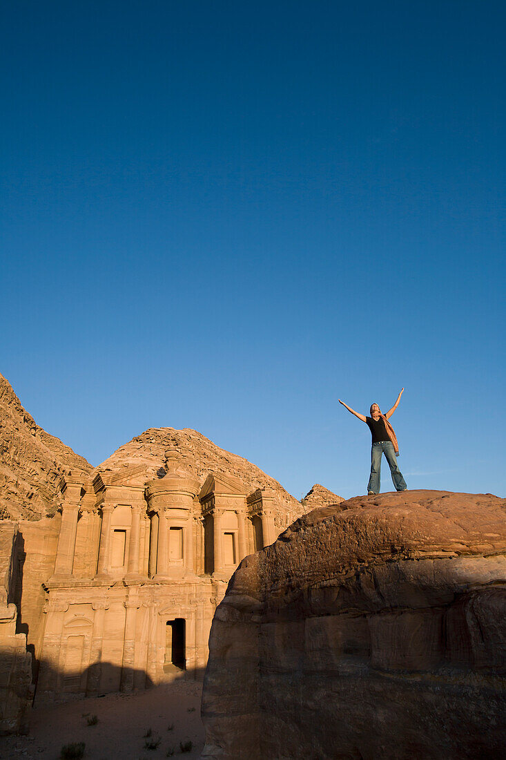 A Woman Tourist Raises Her Arms In Front Of The Nabatean Ruins Of The Monastery; Petra Jordan