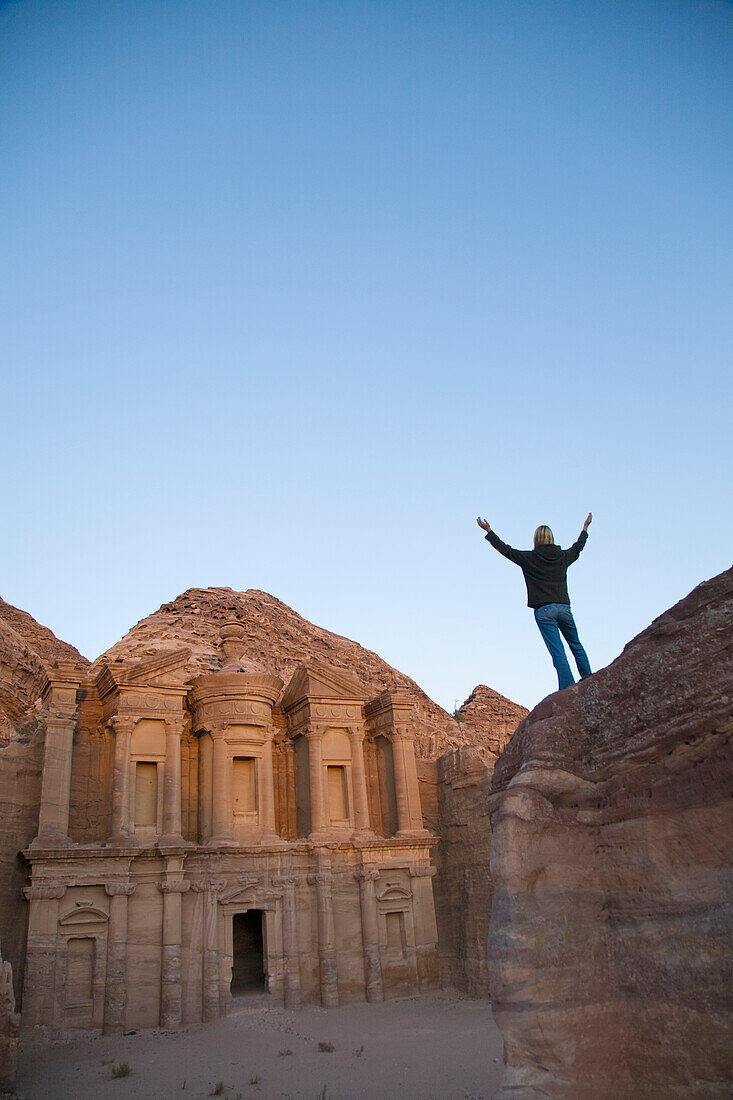 A Woman Tourist Raises Her Arms In Front Of The Nabatean Ruins Of The Monastery; Petra Jordan