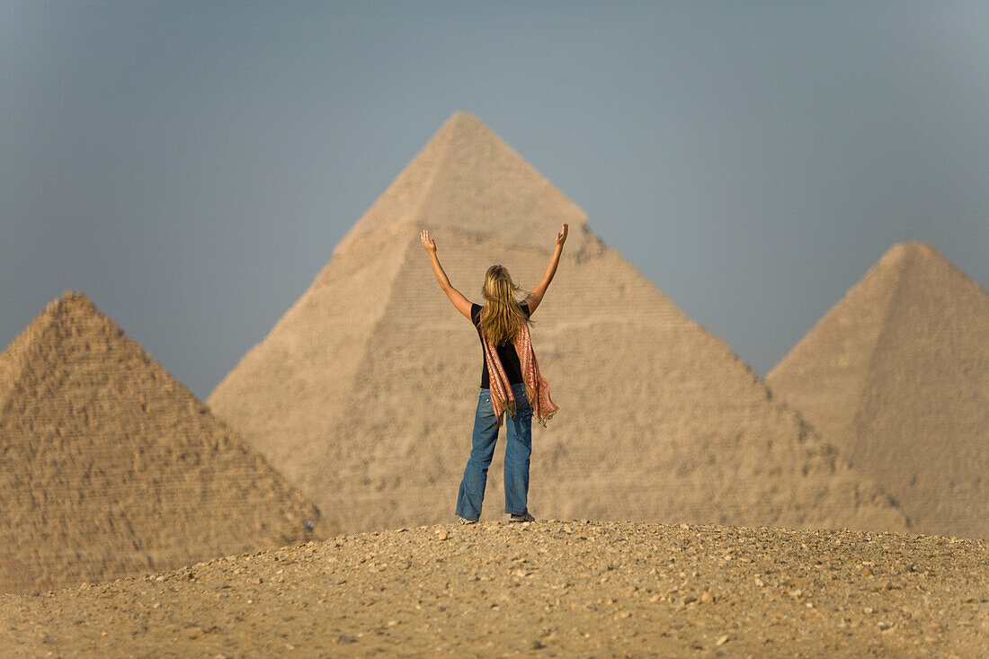 Eine Touristin hebt die Arme und blickt in Richtung der Pyramiden von Gizeh bei Kairo; Gizeh Ägypten
