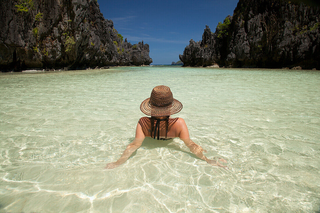 Eine Touristin mit Sonnenhut und Bikini entspannt sich im klaren Wasser der Insel Matinloc bei El Nido und Corong Corong; Bacuit-Archipel Palawan Philippinen