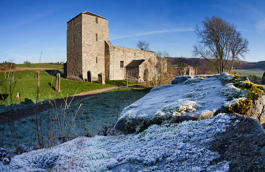 Eine Kirche und ein Friedhof mit Frost auf dem Gras und der Steinmauer; Eglingham Northumberland England