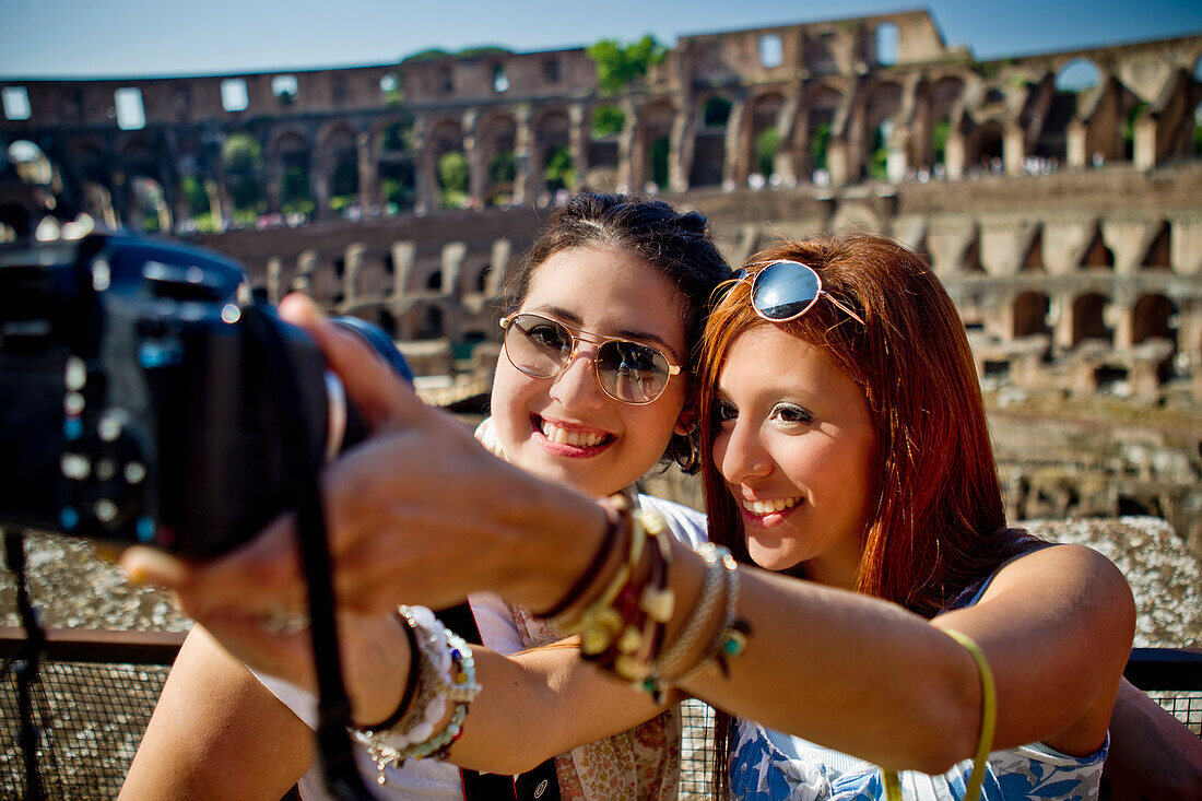 Zwei junge Frauen fotografieren sich selbst mit einer Kamera und dem Kolosseum im Hintergrund; Rom, Italien