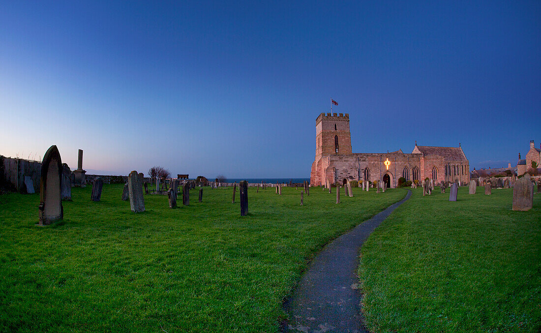 Ein Weg, der durch einen Friedhof zu einem Kirchengebäude führt; Bamburgh Northumberland England