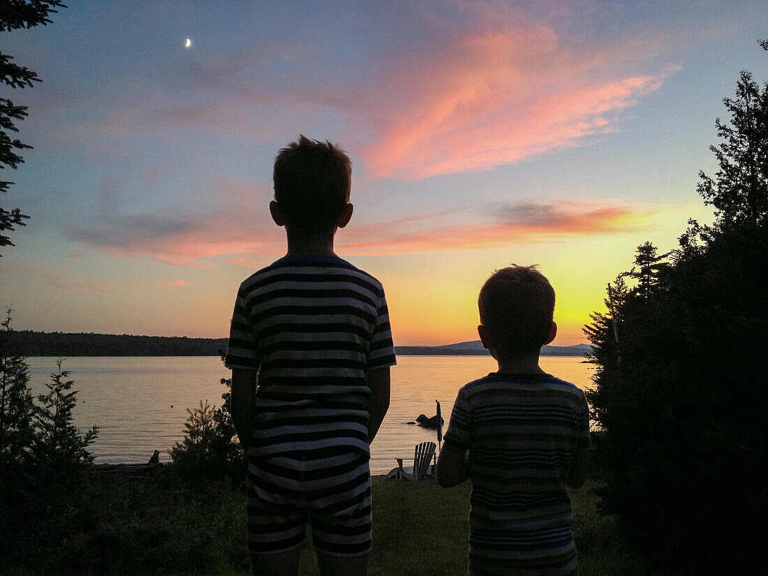 Rückansicht von zwei Jungen, die den Sonnenuntergang am See betrachten