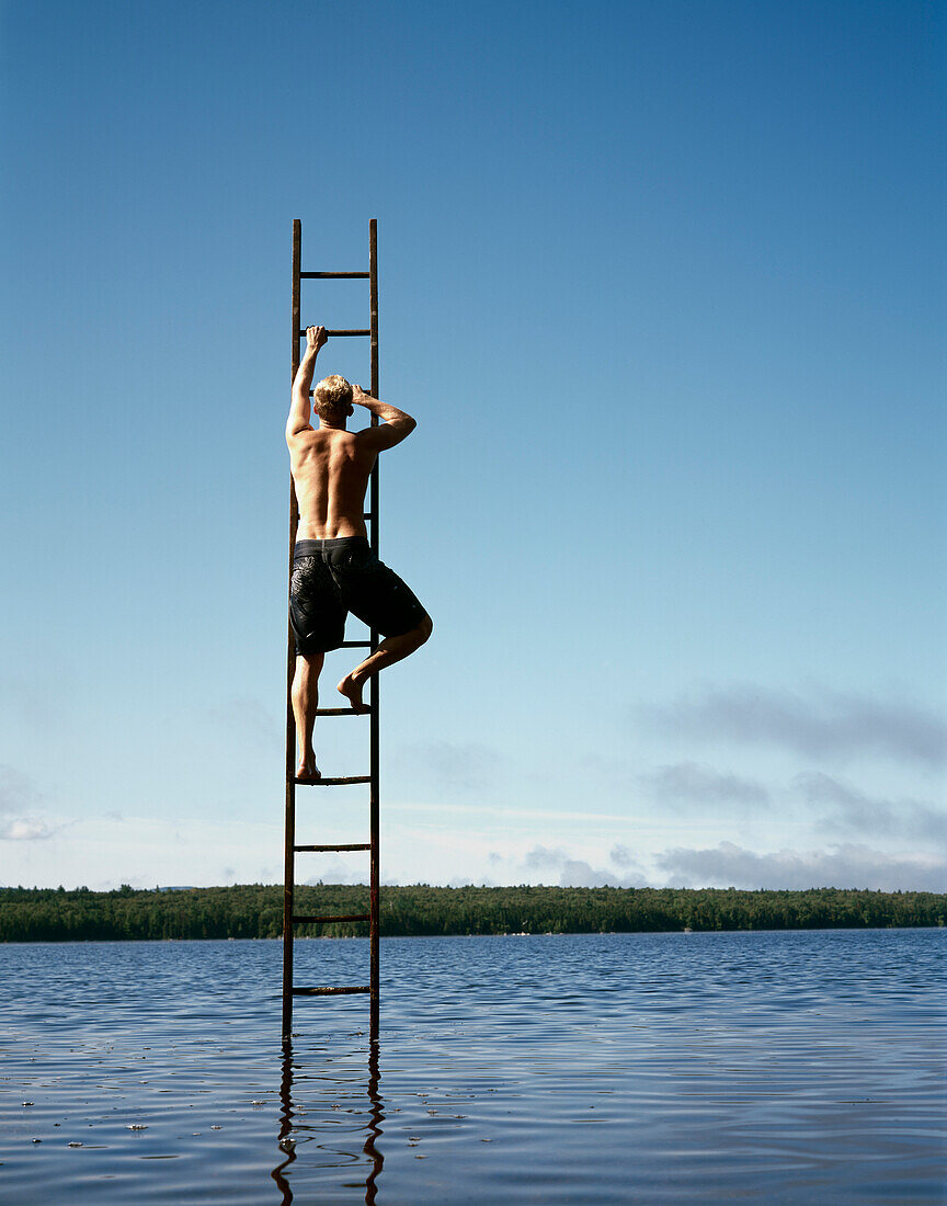 Rückansicht eines mittelgroßen Mannes, der auf eine Leiter in der Mitte des Sees steigt