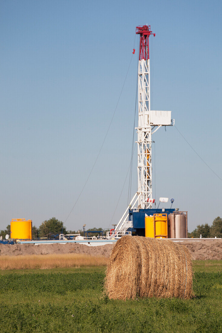 Drilling Rig With Round Hay Bale In The Foreground And Blue Sky; Alberta Canada