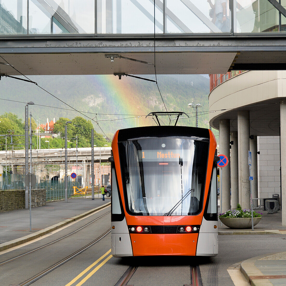 Public Transportation Train On A City Street With A Walkway Overhead And A Rainbow In The Background; Bergen Norway