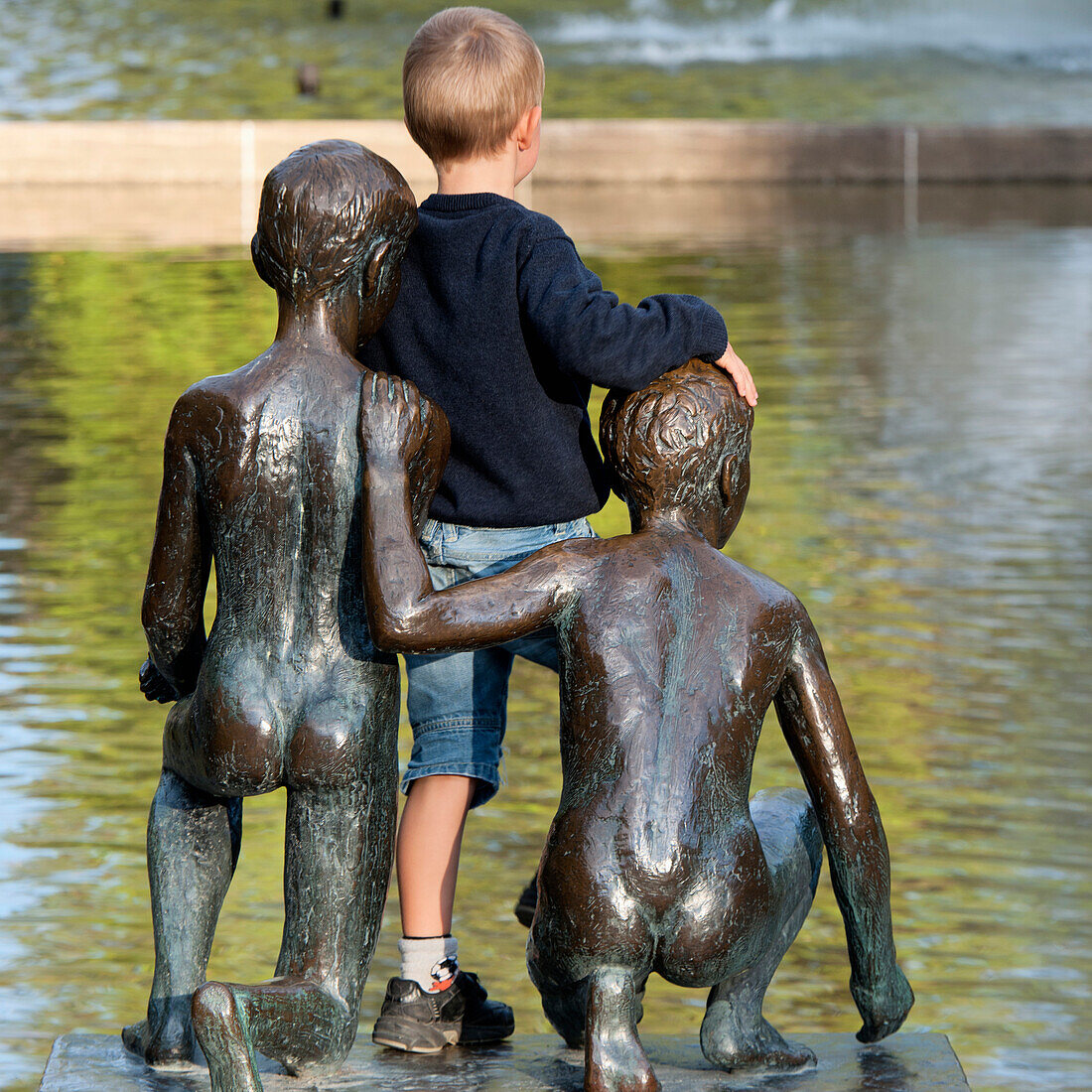 Ein Junge lehnt sich an eine Jungenstatue am Wasser im Spikersuppa-Park; Oslo, Norwegen