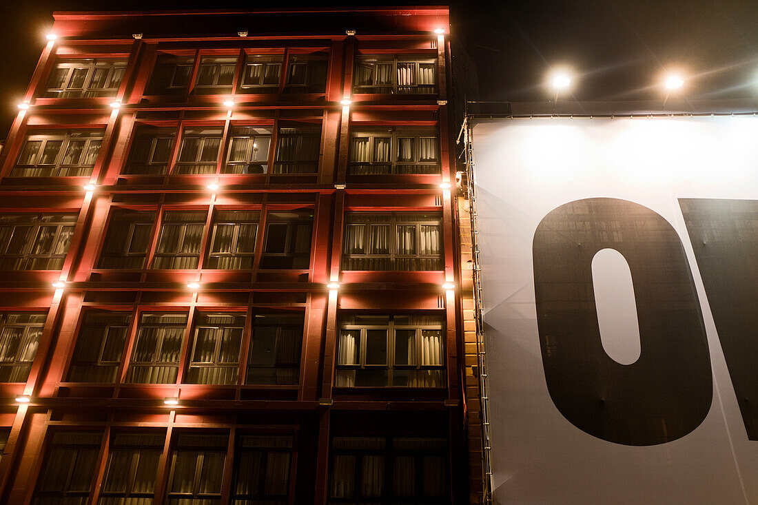 Beleuchtetes Apartmenthaus mit großem Schild bei Nacht, Madrid, Spanien