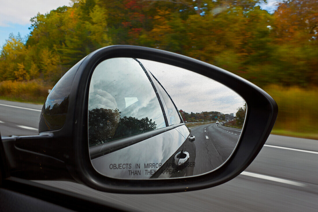 Autoseitenspiegel an der Beifahrertür mit Blick auf Highway und Herbstlaub
