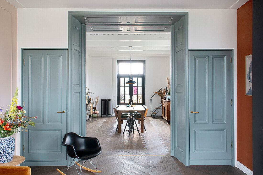 Durchgang mit grau-blauen Holzvertäfelung, flankiert von farblich passenden Türen, mit Blick ins Esszimmer