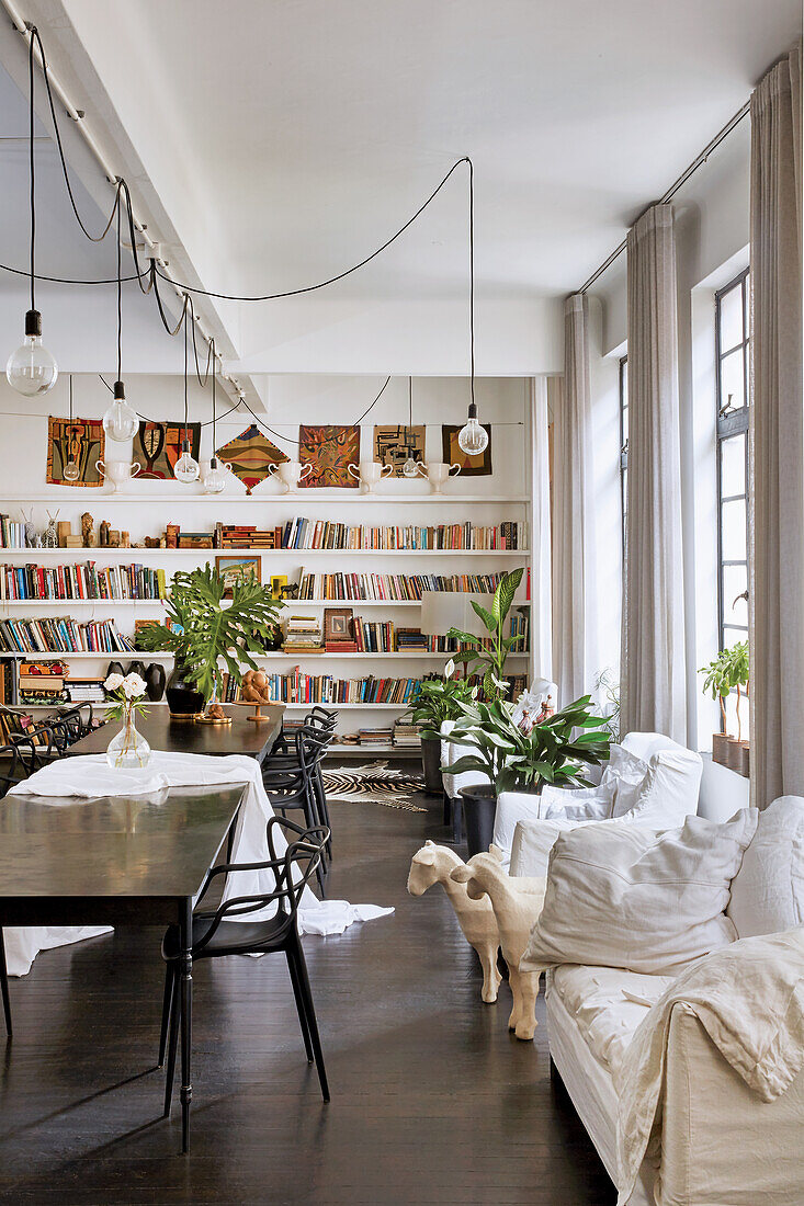 Essbereich mit schwarzen Stühlen und Hussenmöbeln,  im Hintergrund Bücherwand in Loft-Wohnung