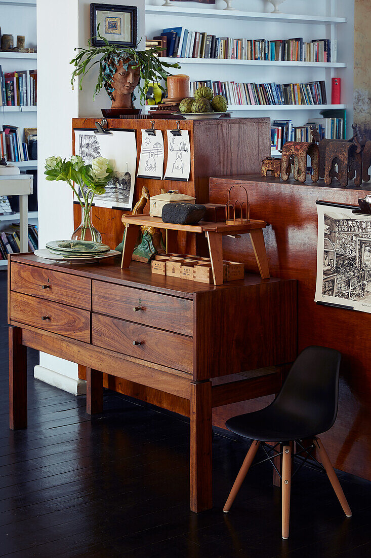 Vintage wooden chest of drawers decorated with art and plants, bookshelf in the background