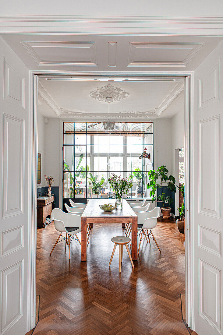 View of wooden table with classic chairs in the old-style dining room with herringbone parquet flooring and glass wall