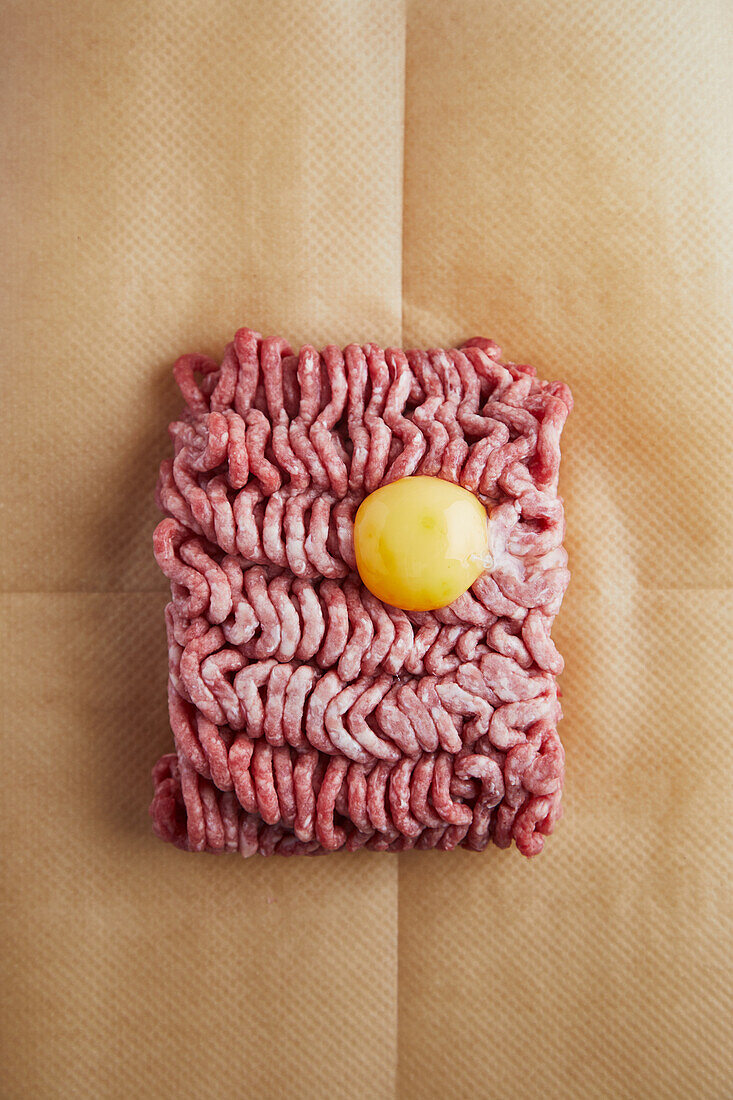 Raw ground meat with egg yolk on brown parchment paper
