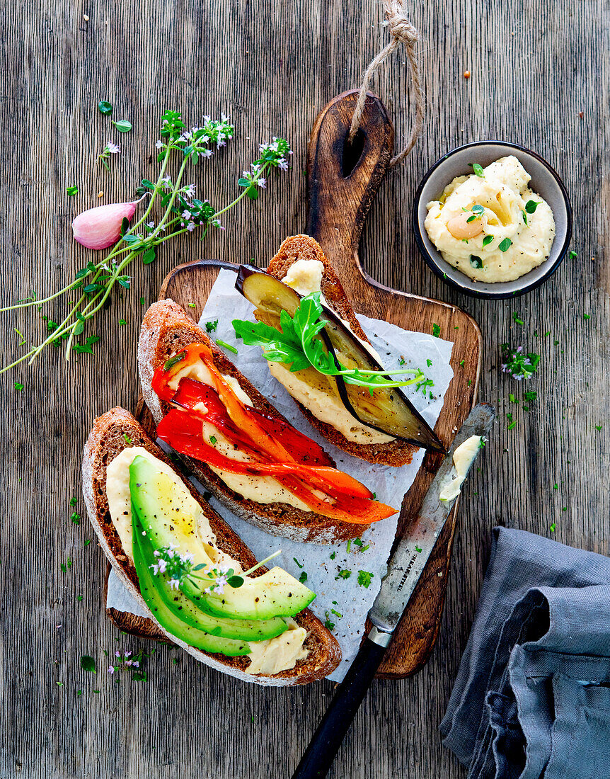 Bread slices with bean puree, avocado, peppers and eggplant