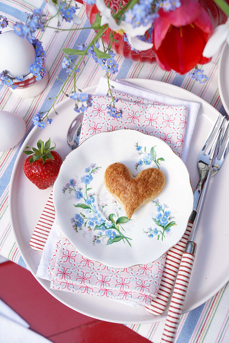 Frühlingshaft gedeckter Tisch mit Herz-Keks und Erdbeere