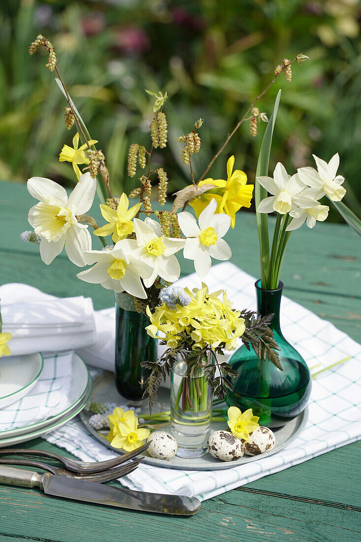 Österliches Arrangement mit Narzissen (Narcissus) und Wiesengräsern auf Gartenholztisch