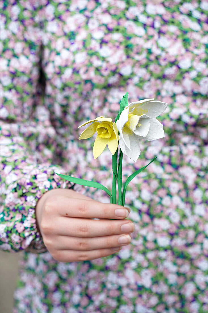 Hand hält DIY-Papier-Narzissen vor gemustertem Kleid