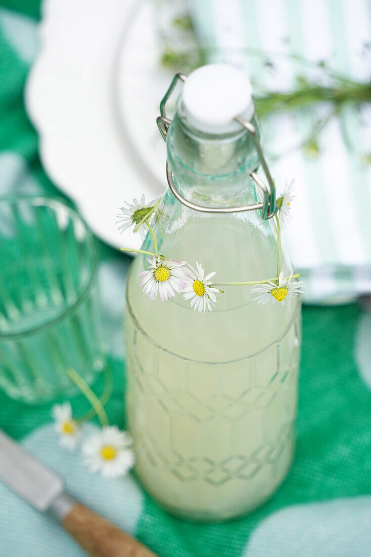 Bügelflasche mit Limonade, verziert mit Kränzchen aus Gänseblümchen